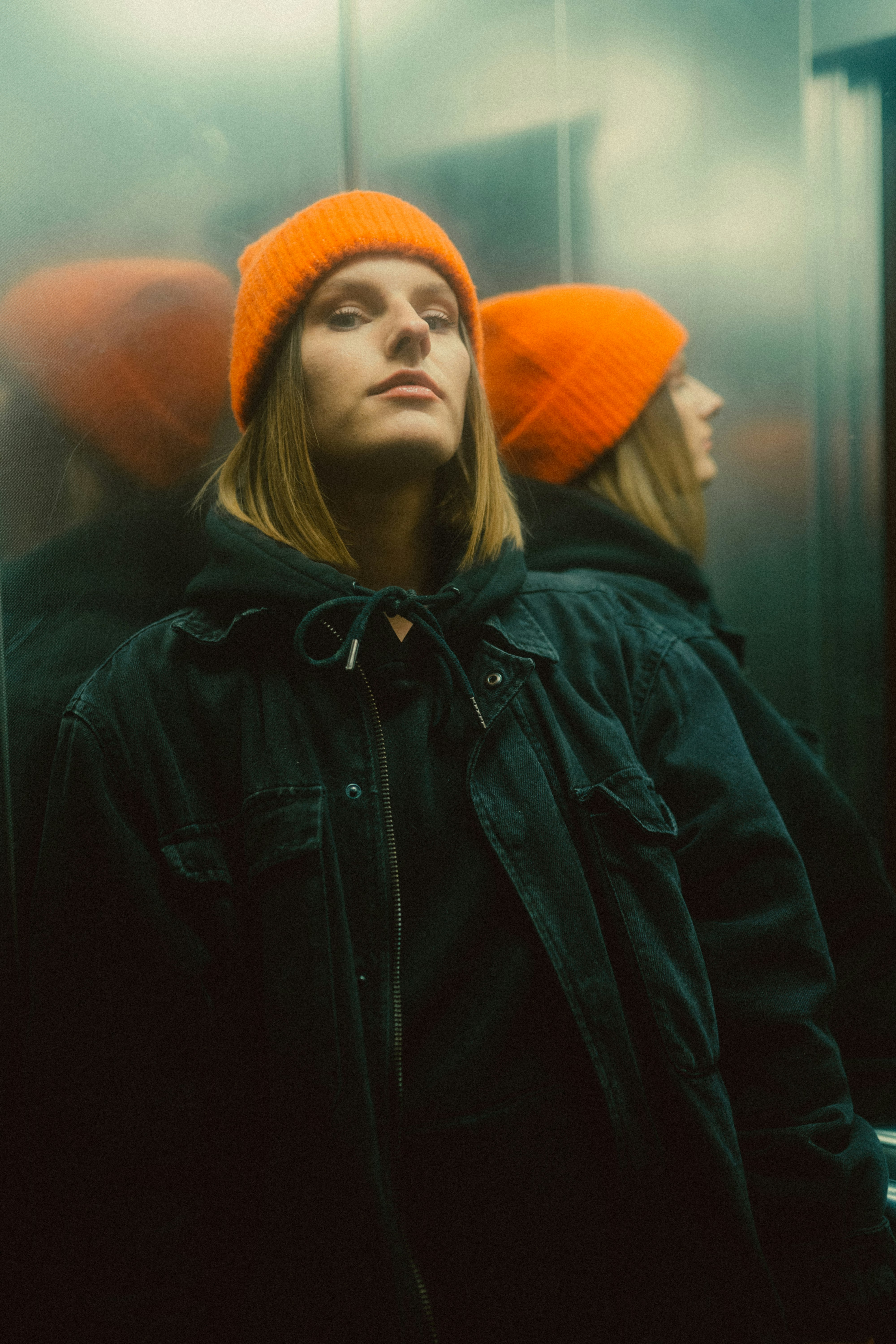 woman in black leather jacket wearing orange knit cap